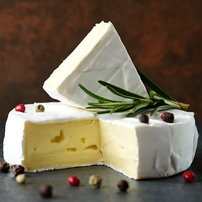 Ein Stück angeschnittener Weichkäse neben Pfefferkörnern