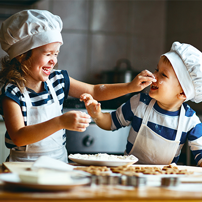 Zwei Kinder beim gemeinsamen Backen und Mehl auf die Nase schmieren