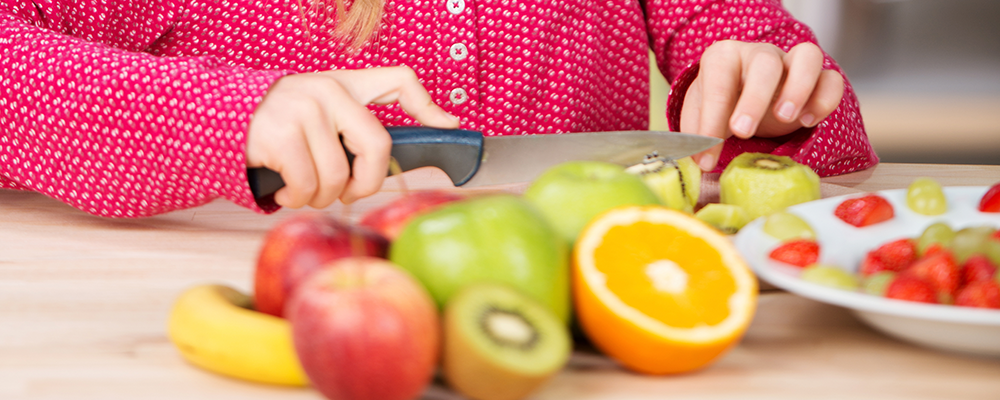 Verschiedenes Obst liegt auf einem Tisch und wird von einem Kind geschnitten