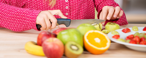 Verschiedenes Obst liegt auf einem Tisch und wird von einem Kind geschnitten