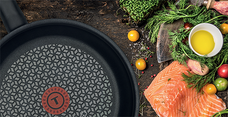 Eine Pfanne, ein Stück roher Lachs und Kräuter