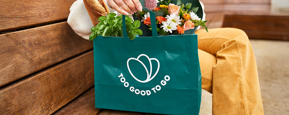 Eine Person mit einem Too Good To Go Sackerl auf einer Parkbank