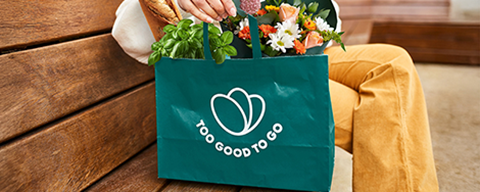Eine Person mit einem Too Good To Go Sackerl auf einer Parkbank
