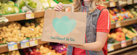 Eine Person mit einem "Too Good To Go"-Karton in der Hand