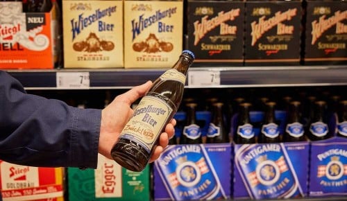 Eine Person steht vor einem Regal und hält eine Bierflasche in der Hand