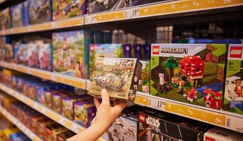 Eine Person steht vor einem Spielzeugregal und hält eine Packung Lego in der Hand