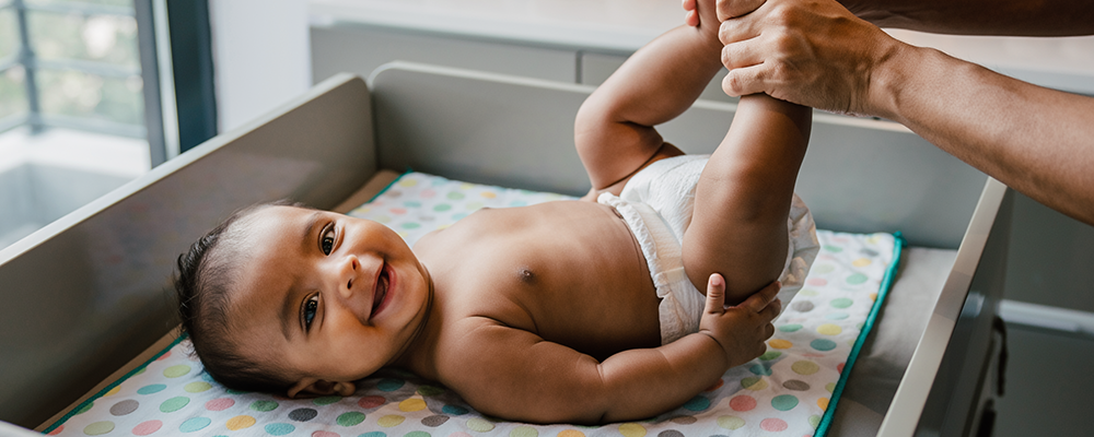 Ein kleines lachendes Baby bei dem gerade die Windel gewechselt wird