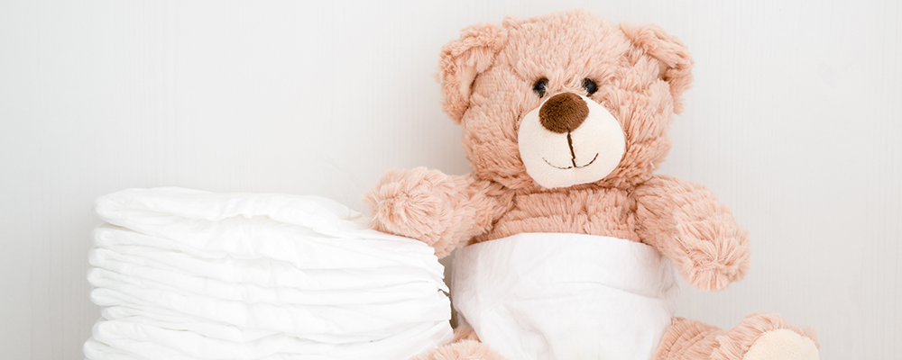 Ein hellrosa Plüsch-Teddybär neben einem kleinen Stapel Windeln
