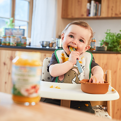 Ein kleines Kind in einem Hochstuhl beim Essen von SPAR Natur*pur Babynahrung