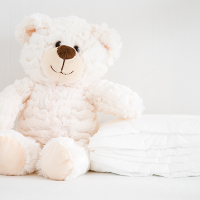 Ein weißer Plüsch-Teddybär neben einem kleinen Stapel Windeln