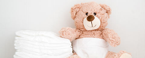 Ein hellrosa Plüsch-Teddybär neben einem kleinen Stapel Windeln