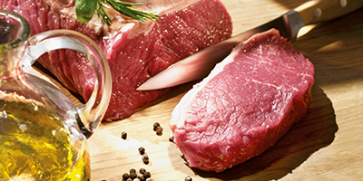 Ein Stück Fleisch, ein Messer und Pfefferkörner auf einem Schneidebrett