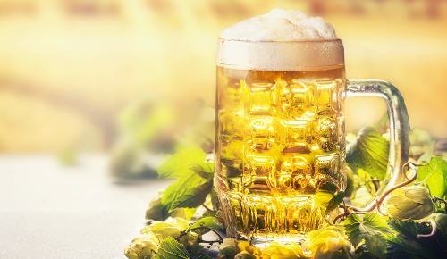Ein voller Bierkrug vor einem sonnigen Weizenfeld im Hintergrund
