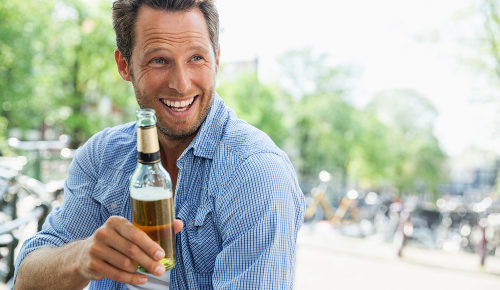 Ein lächelnder Mann mit einen blau-karierten Hemd und einer Bierflasche in der Hand