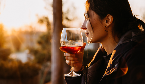 Eine Frau mit einem Glas Rotwein in den Händen schaut sich einen Sonnenuntergang an