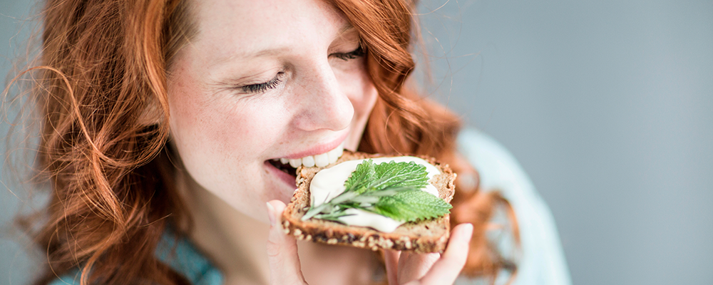 Eine Frau beißt von einer Scheibe Brot mit Frischkäse ab