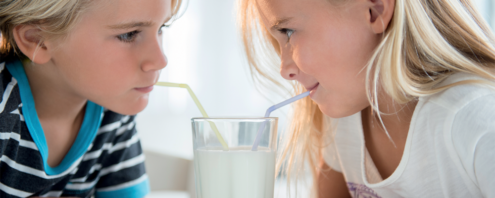 Ein Mädchen und ein Junge trinken mit Strohhalmen aus einem Glas Milch