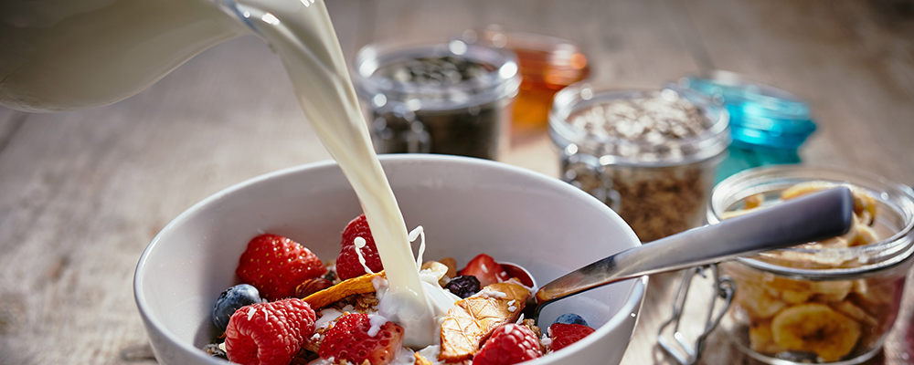 Milch wird in eine Schale mit Müsli und Beeren gegossen