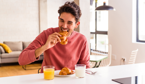 Ein Mann beim Frühstück beißt in ein Croissant