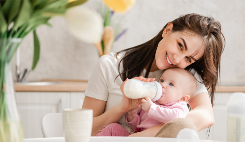 Eine Mutter mit einem Baby auf dem Schoß, das aus einer Flasche trinkt