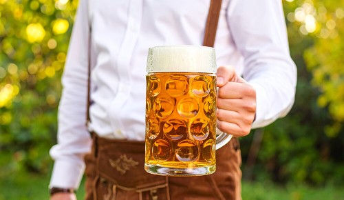 Eine Person in Lederhose hält einen vollen Masskrug in den Händen