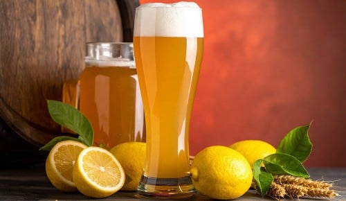 Ein Bierglas gefüllt mit Radler neben ganzen und halben Zitronen
