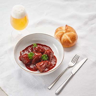 Ein Teller Gulasch mit einer Semmel und einem Glas Bier