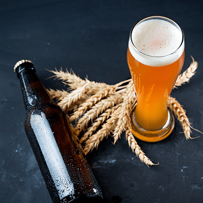 Ein Glas Weißbier neben einer Bierflasche und Weizenähren