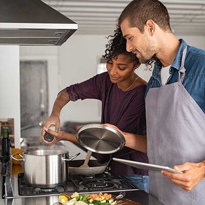 Frau und Mann kochen in einer Küche. Frau würzt das Gericht und der Mann schaut zu