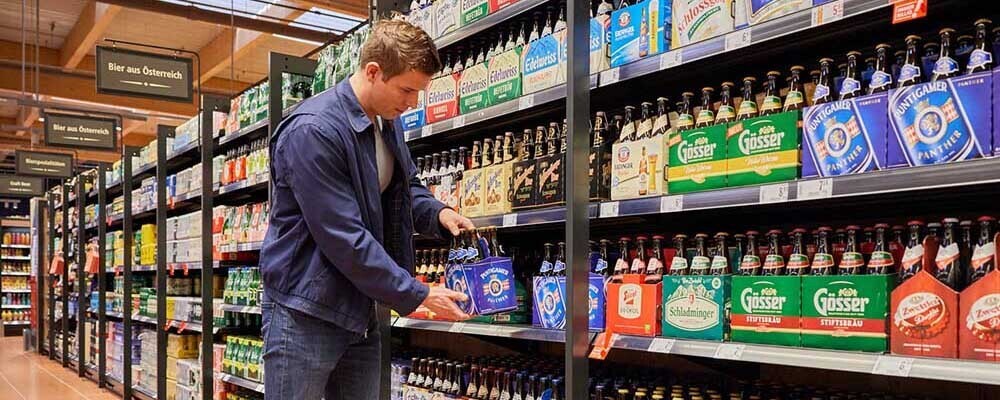 Ein Mann nimmt ein 6er-Tragerl Bier aus einem Regal