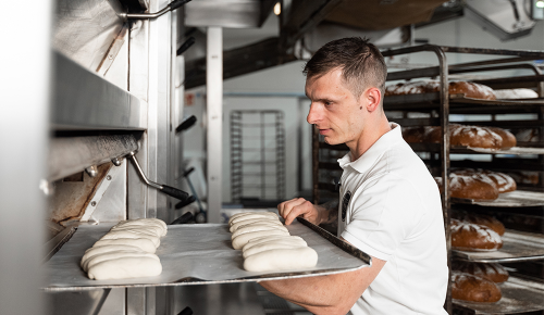 Ein INTERSPAR-Bäcker schiebt ein Blech voller frische Bäckerzeilen in den Ofen