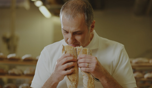 Ein Bäcker riecht genüsslich an einem aufgebrochenen, frisch gebackenen Baguette