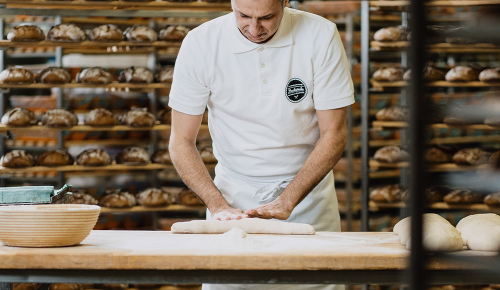 Ein Bäcker beim ausrollen eines Baguettes mit frischem Teig