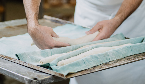 Ein frischer Baguette-Teig wird in eine Form mit Geschirrtüchern gelegt