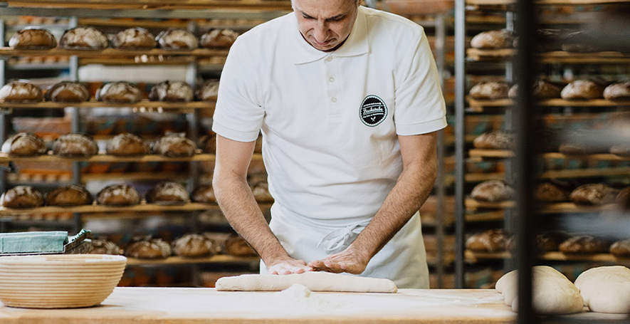 Ein Bäcker beim ausrollen eines Baguettes mit frischem Teig