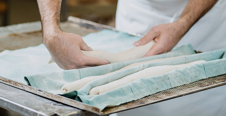 Ein frischer Baguette-Teig wird in eine Form mit Geschirrtüchern gelegt