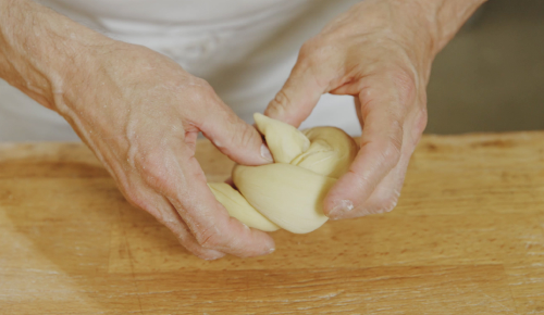 Ein/e Bäcker:in formt einen Brioche-Knopf aus einem Teig