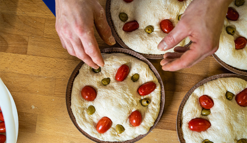 Eine ungebackene Focaccia mit Tomaten und Oliven in einer Form