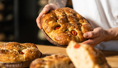 Frisch gebackene Focaccia mit Oliven und Tomaten in einer Pappform