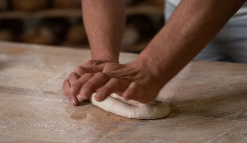 Ein/e Bäcker:in beim Formen eines Baguettes