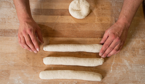 Mehrere in Stangengeformte Baguette-Teiglinge auf einem Holzbrett