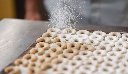 Ein Blech voller frischer Vanillekipferl wird mit Staubzucker bestreut
