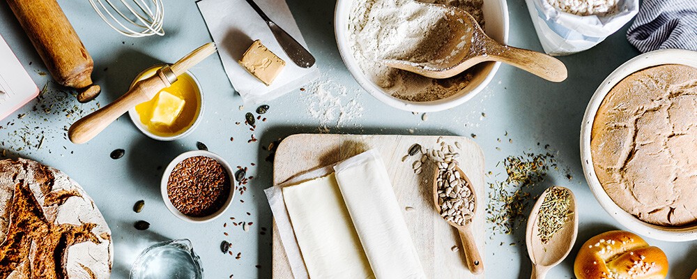 Mehrere Utensilien und Zutaten zum Backen auf einem hellblauen Untergrund