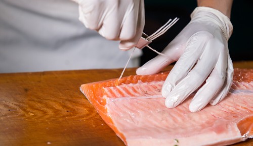 Eine Person mit weißen Handschuhen beim Entgräten eines Stück Lachs