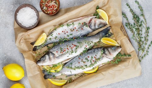 Drei garnierte frische Fische mit Gewürzen und Zitronen in einem Backblech