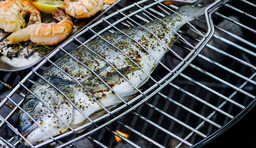 Eine gegrillte Dorade in einem Grillgitter auf einem Kugelgrill