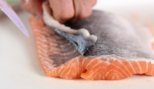 Eine Person beim Entfernen der Haut von einem Stück Lachs