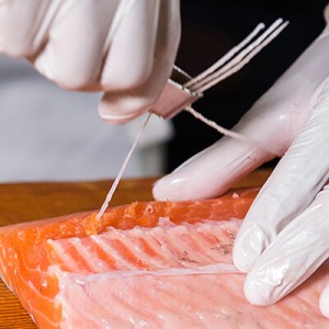 Eine Person mit weißen Handschuhen beim Entgräten eines Stück Lachs