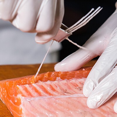 Eine Person mit weißen Handschuhen beim Entgräten eines Stück Lachs