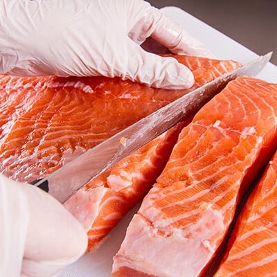 Eine Person mit weißen Handschuhen beim Schneiden eines Stück Lachs